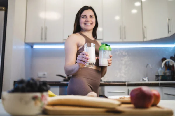 Foto colorida de mulher segurando copo de leite e coqueteleira - Metrópoles