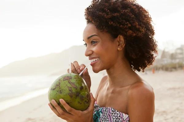 Mulher negra bebendo água de coco em praia
