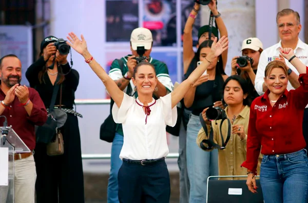 Imagem colorida mostra Claudia Sheinbaum de braços abertos durante evento no México - Metrópoles