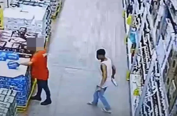 Imagem colorida de um homem com uma garrafa de bebidas na mão andando em direção a outro homem com camiseta vermelha - Metrópoles