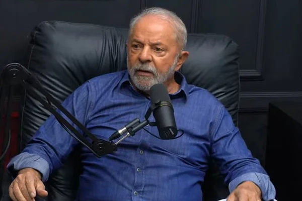 Lula com camisa social azul sentado em cadeira preta e falando em microfone