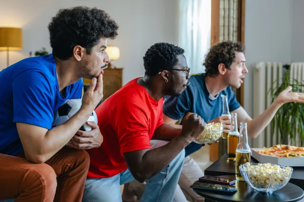 Foto de três homens assistindo a jogo de futebol - Metrópoles
