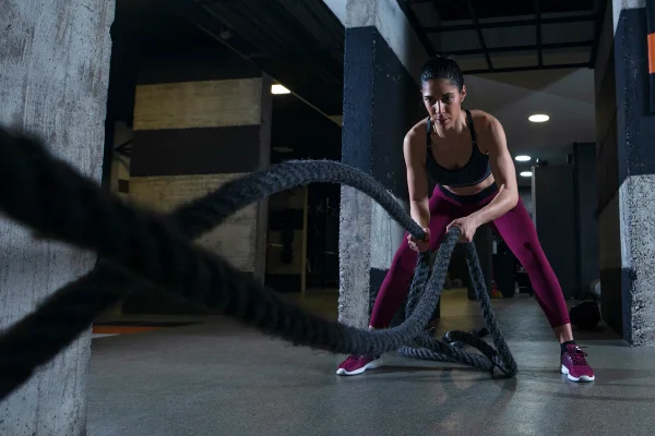 Mulher praticando exercícios com cordas navais na academia. Metrópoles