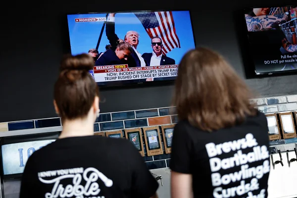 Pessoas veem imagens de um ex-presidente dos EUA ferido e candidato presidencial republicano Donald Trump enquanto assistem ao noticiário da televisão no The New Fashioned do outro lado da praça do Fórum Fiserv em 13 de julho de 2024 em Milwaukee, Wisconsin