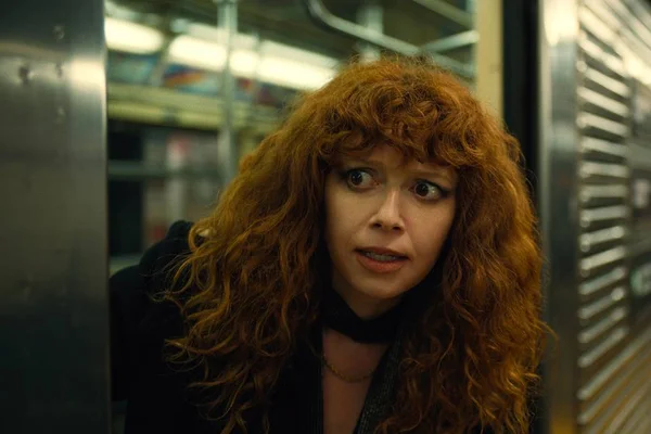 Mulher de cabelo vermelho cacheado com a cabeça fora do trem do metrô