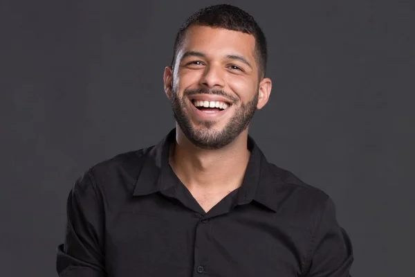 Jonas Nascimento, maquiador brasiliense. Ele é pardo, tem cabelo e barba curta e escura e sorri sob fundo cinza escuro - Metrópoles