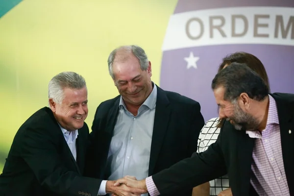 Sob fundo da bandeira do Brasil, Rodrigo Rollemberg (PSB), Ciro Gomes (PDT) e Carlos Lupi (PDT) se cumprimentam e sorriem. Eles usam terno - Metrópoles