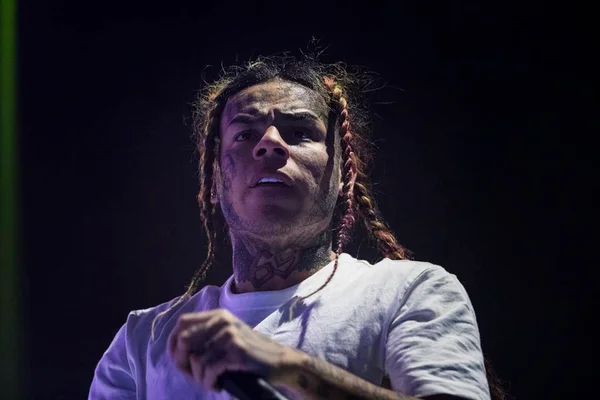 Foto de um homem branco, com tatuagens no rosto, cabelo colorido trançado, usando blusa branca e segurando um microfone - Metrópoles