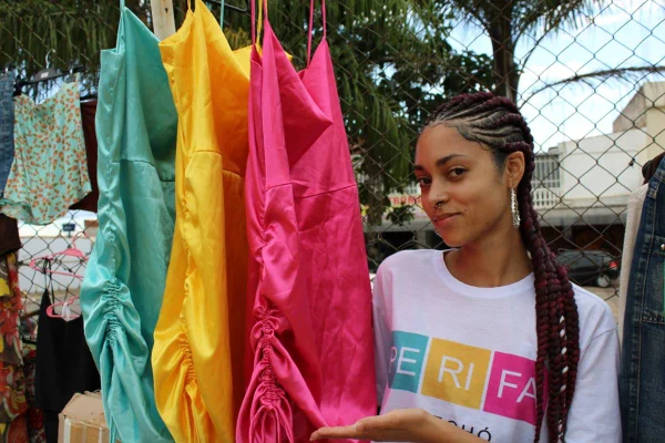 Mulher ao lado de arara com roupas coloridas