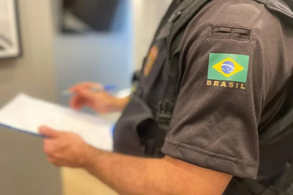 Imagem colorida mostra tronco de homem vestindo uniforme da PF com camisa preta com bandeira do Brasil bordada no braço - Metrópoles