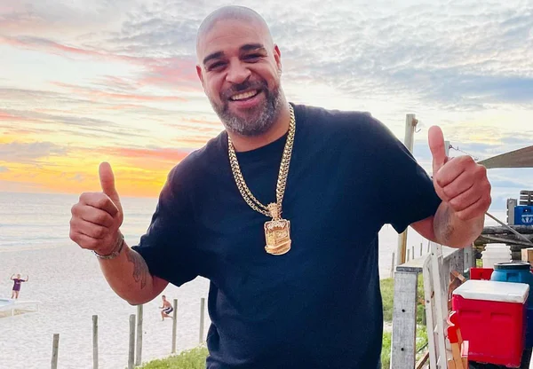 Adraino, ex-jogador de futebol. Ele está ao ar livre, com camisa azul, bermuda branca e colar de ouro - Metrópoles