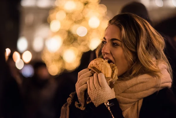Garota despreocupada saboreando um pedaço de cheeseburger. Metrópoles