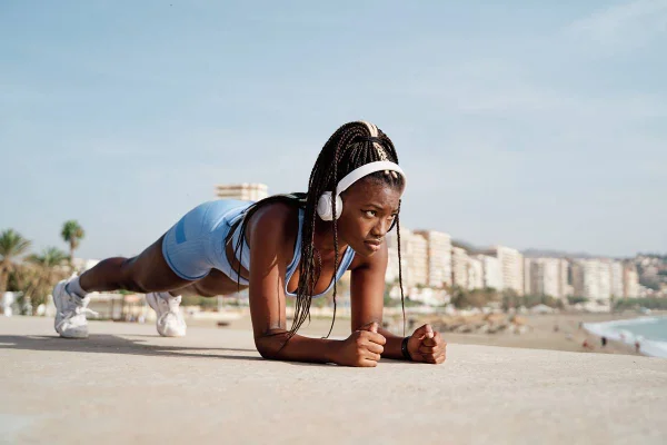 Foto colorida de uma mulher com roupa azul e fones de ouvidos brancos fazendo exercício físico - Metrópoles
