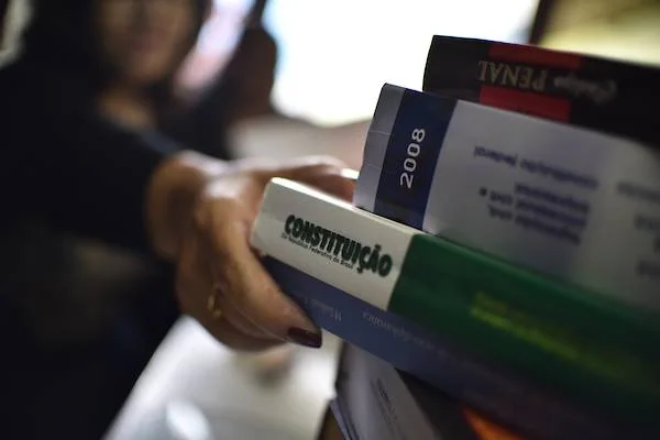 foto colorida de uma mão puxando livros de uma prateleira