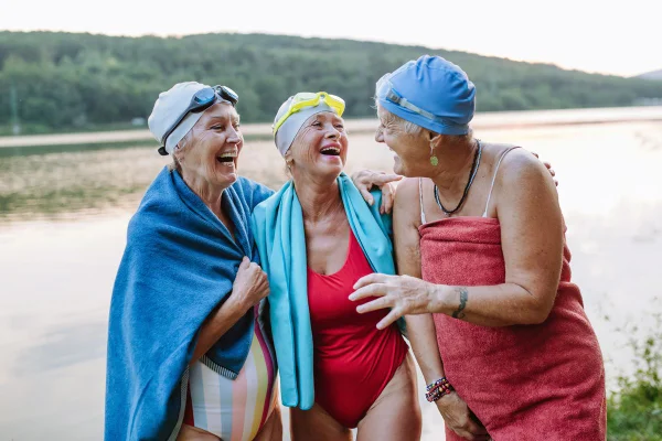 Foto colorida de três mulheres sorridentes e com roupa de banho no treino de natação - Metrópoles
