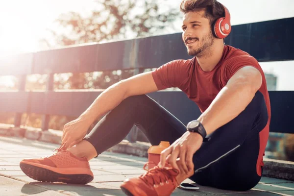 Corredor sentado no chão com roupa de academia e tenis com fone de ouvido - Metrópoles - autocudiado, gentil consigo mesmo