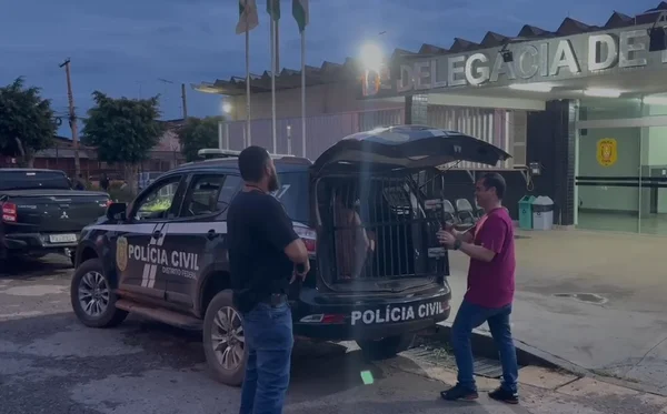 Imagem colorida de um homem dentro de uma viatura em frente a uma delegacia de polícia- Metrópoles