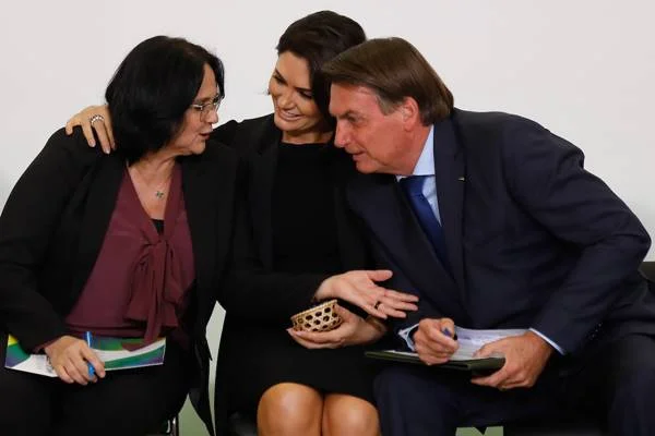 Fotografia colorida mostra duas mulheres e um homem sentados conversando