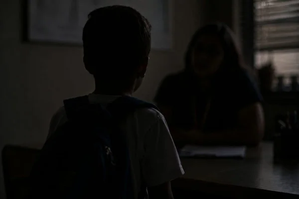 Imagem criada por IA mostra menino com mochila nas costas conversando com professora