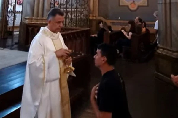 Imagem colorida de homem ajoelhado perante padre. Metrópoles