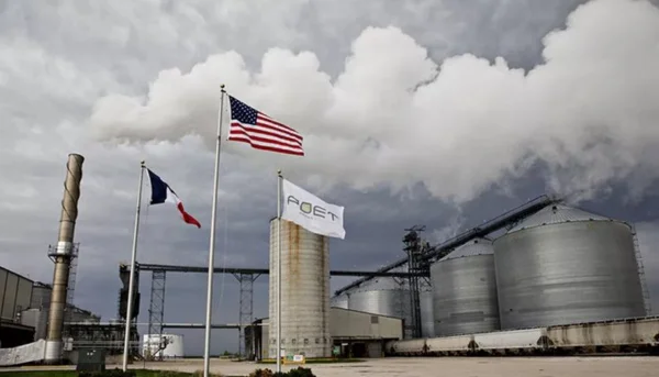 foto de uma fábrica com grandes construções na cor cinza. se v~e a bandeira dos estados unidos e da frança