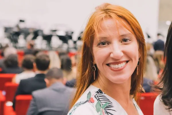 Imagem colorida de ruiva sorrindo com público ao fundo