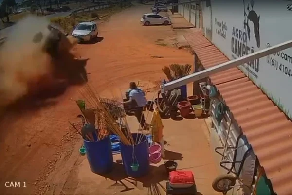 Carro capotando, barro e poeira no ar e mulher em frente a casa