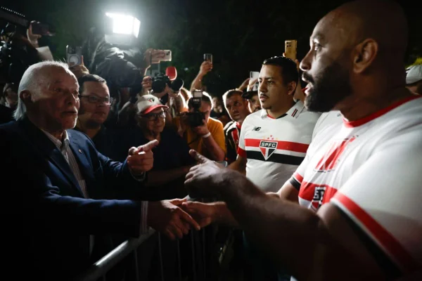 Imagens coloridas mostram homem branco, calvo e com barba, sorrindo e cumprimentando homens com a camisa do São Paulo FC durante protesto na frente do Morumbis