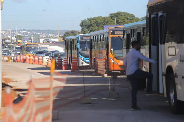 Foto colorida de homem subindo em ônibus em meio a trânsito intenso de veículos devido a obras