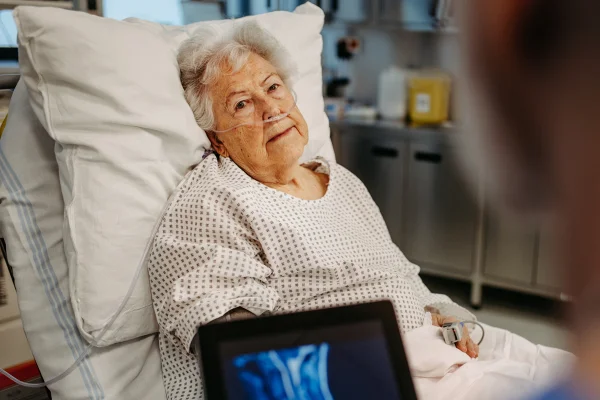 Foto colorida de mulher idosa em maca de hospital próximo a uma radiografia - Metrópoles