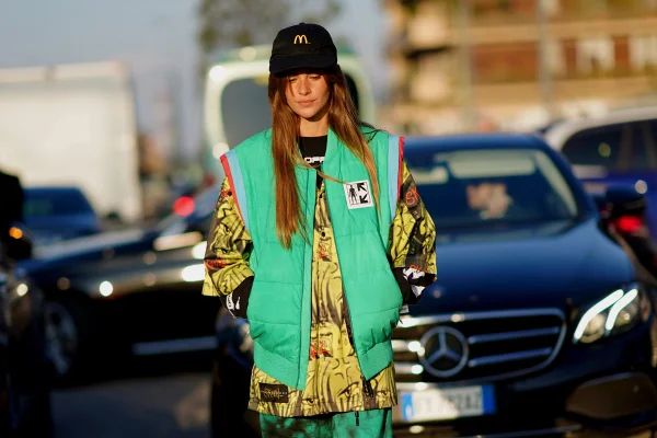 Mulher branca com colete verde andando na rua