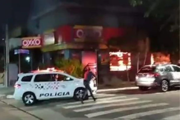 Imagem colorida mostra unidade do mercado Oxxo pegando fogo com carro de polícia na frente; homem acusado pelo incêndio foi preso - Metrópoles