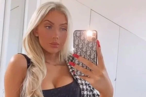 Mulher branca e loira posando para foto tirada no espelho com o próprio celular