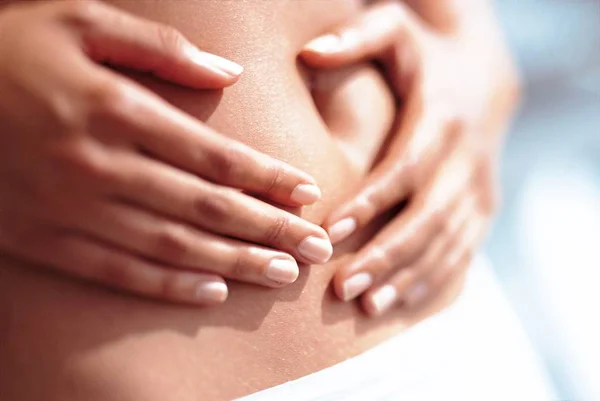 Foto em close de uma mulher com as duas mãos segurndo a barriga - Metrópoles