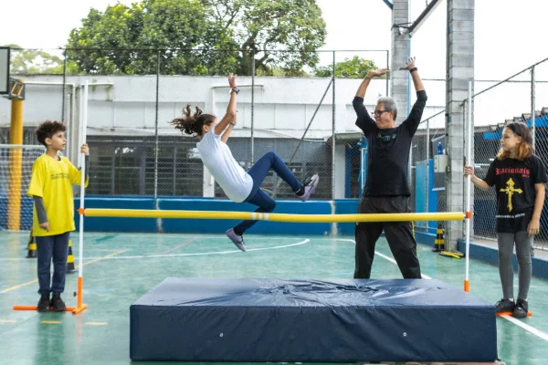 imagem colorida mostra criança saltando sobre vara em quadra de escolas - metrópoles