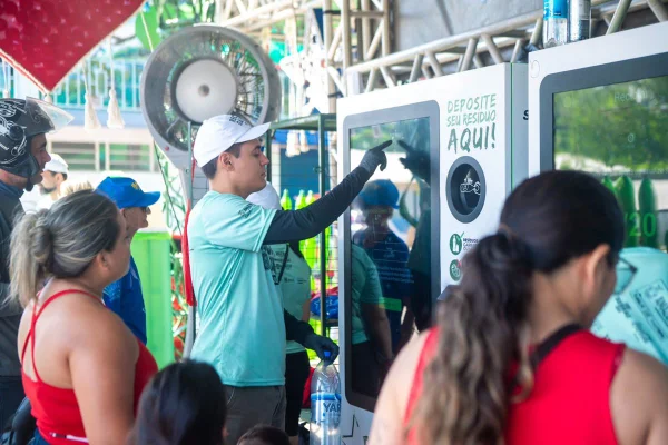 Foto colorida de pessoas depositando garrafas em totens