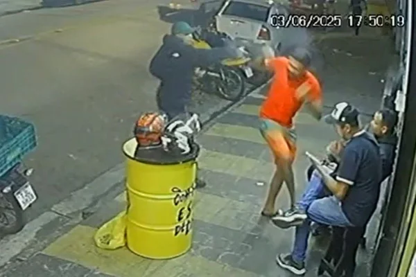 Homem de boné verde e jaqueta preta aponta arma para outro homem, de camiseta laranja - Metrópoles