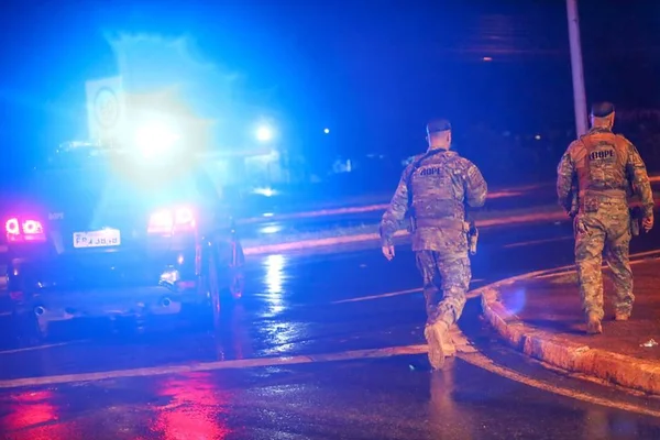 Policiais militares fardados, em Brasília. A foto colorida tem luzes e ocorreu à noite