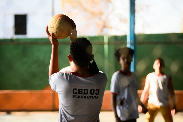 estudante de costas com uniforme do CED 3 arremessa bola