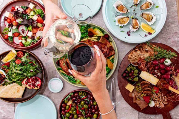 Mesa ista de cima com várias comidas e duas pessoas brindando - Metrópoles