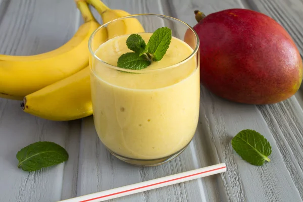 Foto de stock de Smoothie de manga e banana no fundo de madeira cinza