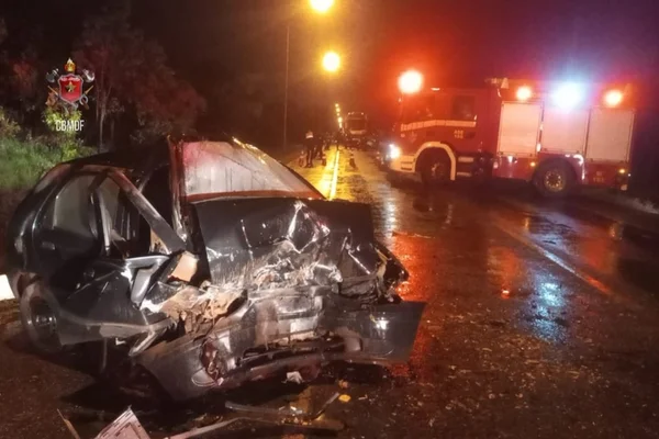 Ferragens de carro preto que colidiu contra outro veículo na DF-128. Ao fundo, caminhão do CBMDF. Noite, com pista molhada e iluminada por postes - Metrópoles