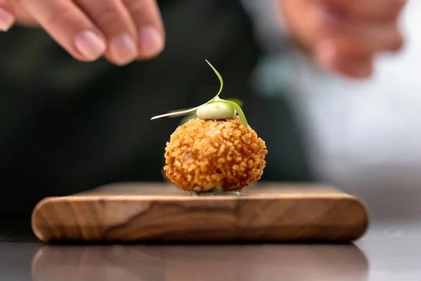Foto colorida de um croquete de vatapá em cima de uma tábua de madeira - Metrópoles