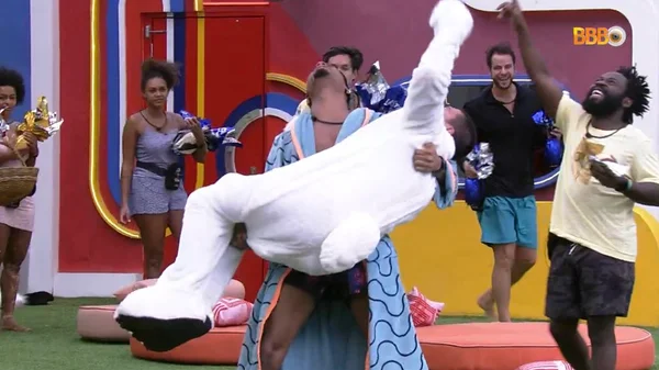 Arthur Aguiar no colo de PA, participantes do BBB22, após o primeiro voltar do paredão falso enquanto outros brothers assistem a comemoração - Metrópoles