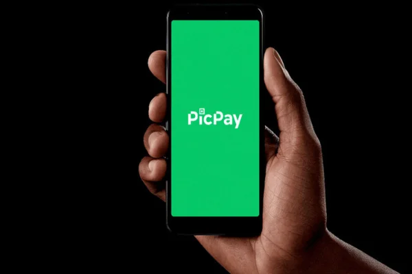 Imagem de pessoa segurando um celular com a imagem da logomarca do PicPay - -Metrópoles