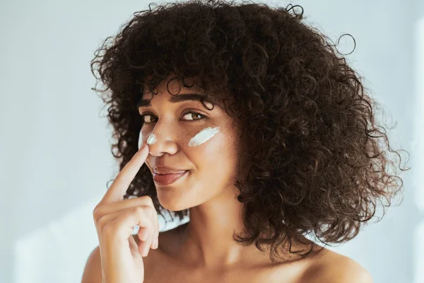 Foto colorida - mulher com cabelo cacheado usando protetor solar na pele