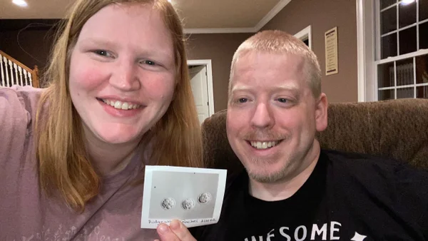foto colorida de casal feliz segurando imagem de três embriões