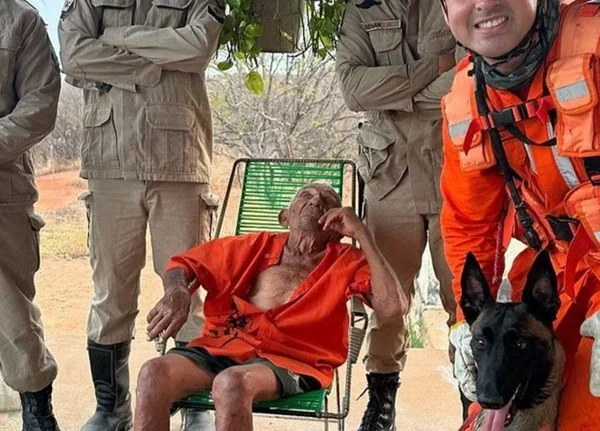Foto colorida de idoso sentado ao lado de bombeiros e cachorro - Metrópoles