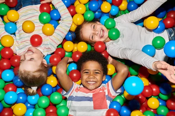 Na foto, três crianças sorrindo deitadas em uma piscina de bolinhas - Metrópoles