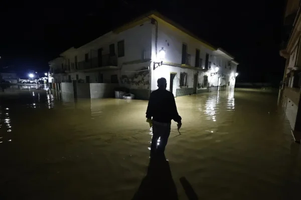 Foto colorida de homem em rua completamente alagada após temporal na Espanha